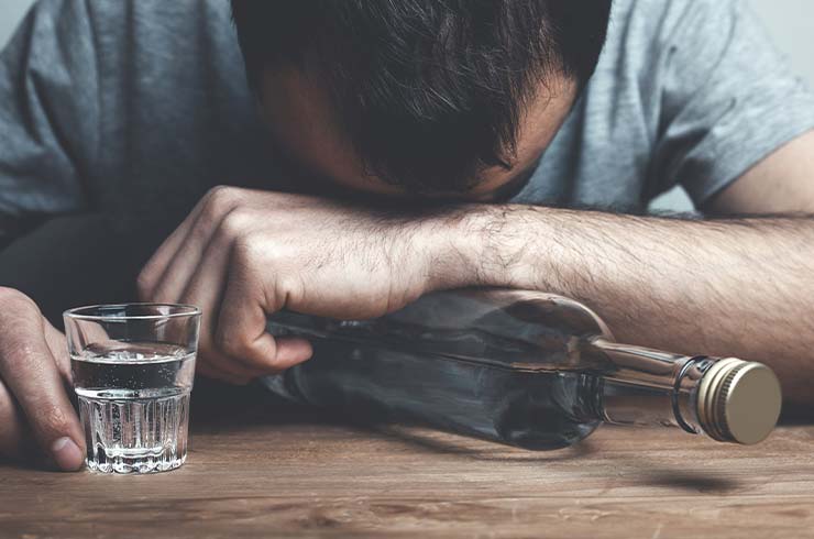 man with his head down on a table with a glass and bottle of liquor experiencing alcohol withdrawal